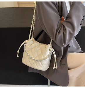 Détail d'un sac seau matelassé crème avec poignée en perles et chaîne sur un modèle