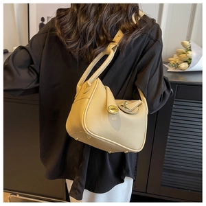Sac seau en cuir beige grainé avec fermoir rotatif doré porté par le mannequin