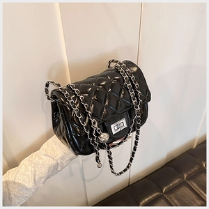 Detail of black quilted crossbody bag with silver chain strap and metal turn-lock