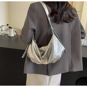 Detail of silver crocodile embossed leather hobo bag worn over the shoulder on a brown blazer