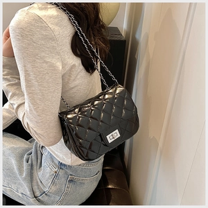 Detail of black quilted leather shoulder bag with silver chain strap worn by a model