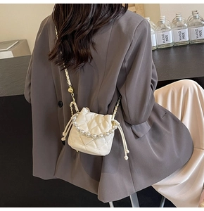 Détail du sac seau matelassé blanc avec anse en perles et chaîne à boule dorée