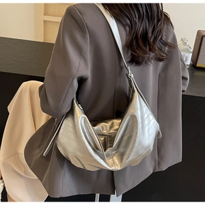 Detail of silver metallic crescent bag with crocodile texture worn by a model