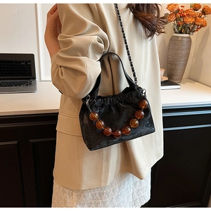 Dettaglio borsa a secchiello in velluto nero con perle ambra e catena chic