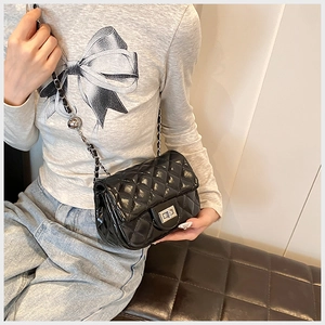 Detailed view of black quilted crossbody bag with silver chain and decorative metal ball