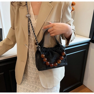 Detail of black pleated faux suede handbag with amber bead chain on a model in a beige suit