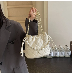 Détail du sac seau matelassé crème avec chaîne en perles et écusson logo mode