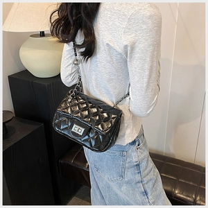 Detail of classic black quilted shoulder bag with silver chain strap on model