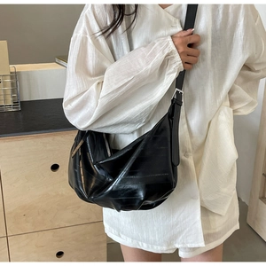 Detail of black crescent crossbody bag with pleated texture on model's shoulder