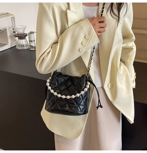 Gros plan d'un sac seau matelassé noir avec poignée en perles et logo en métal