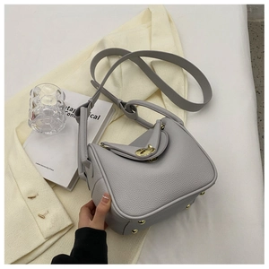 Détail d'un sac seau en cuir gris avec fermoir métallique doré et rivets de protection