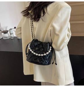 Détail du sac seau noir matelassé avec accent perle et bandoulière chaîne porté