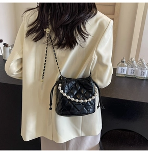 Détail du sac seau noir matelassé avec poignée en perles et bandoulière sur un blazer