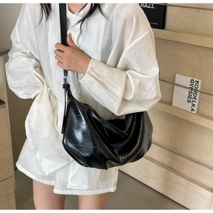 Detail of black glossy crescent shoulder bag with pleated texture on white shirt model