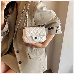 Detail of white quilted leather chain bag with silver twist lock on beige blazer