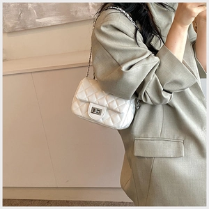 Side view of white quilted chain bag with silver clasp worn with a blazer
