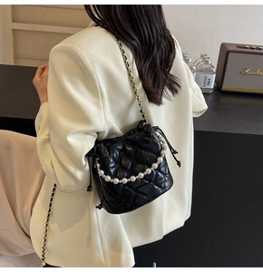 Détail d'un sac seau noir matelassé avec chaîne en perles et bandoulière porté par un mannequin