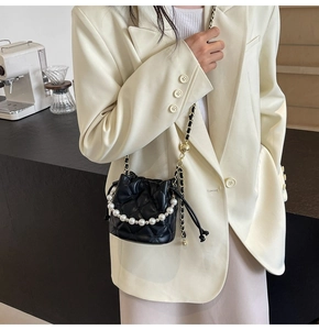 Détail d'un sac seau matelassé noir avec poignée en perles et bandoulière en chaîne cuir