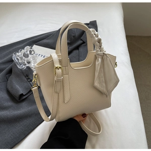 Detail of minimalist cream bucket bag featuring lychee grain leather and silk scarf handle