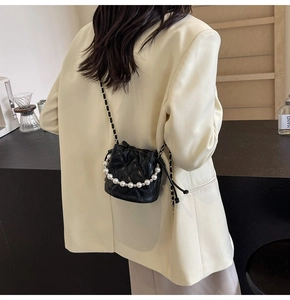 Sac seau noir matelassé avec poignée perle porté sur l'épaule d'un blazer blanc