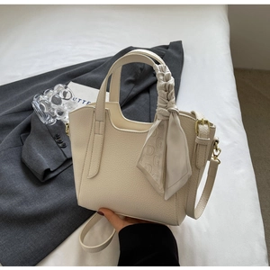 Detail of cream pebbled leather bucket bag with decorative silk scarf and long strap
