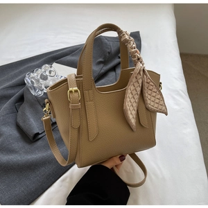Detail of khaki pebbled leather bucket bag with decorative silk scarf and gold hardware