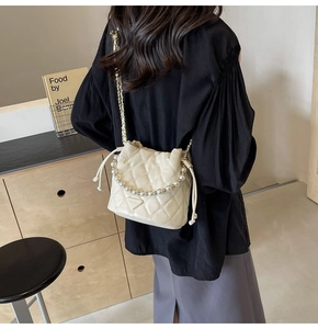 Détail d'un sac seau matelassé beige avec poignée en perles et chaîne dorée sur mannequin