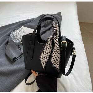 Detail of black pebbled leather bucket bag featuring a decorative silk scarf and gold hardware