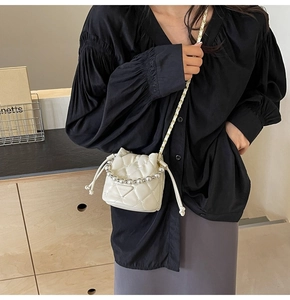 Détail d'un sac seau matelassé blanc crème avec poignée en perles et bandoulière