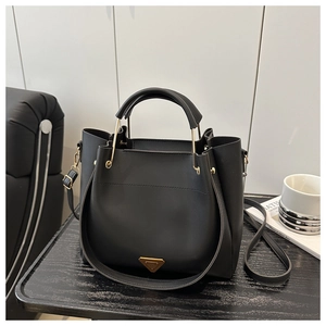 Detail of black bucket handbag with gold metal handle and logo plate on wood surface