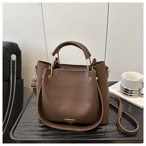 Detail of dark brown bucket handbag with gold metal hardware and adjustable shoulder strap