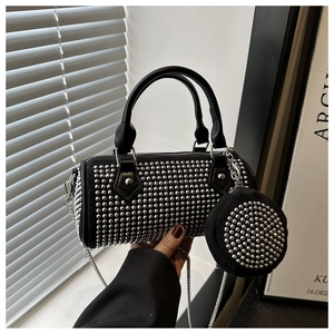 Detalle de bolso cilíndrico negro con tachuelas, cadena y mini monedero redondo