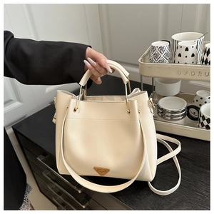 Detail of cream white leather bucket bag featuring a gold triangle metal logo and handle