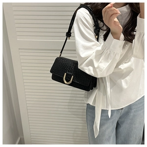 Detail of black crocodile pattern crossbody bag with a gold horseshoe metal buckle