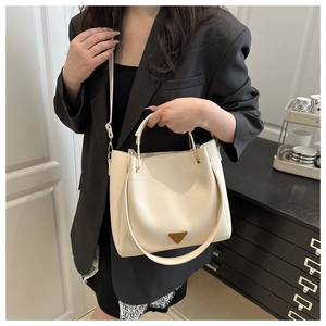 Detail view of the cream white bucket bag with round metal handle and triangle logo plaque