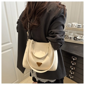 Detail of cream white bucket bag featuring metallic handles and elegant triangle plaque