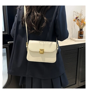 Detail of cream white leather crossbody bag with vintage gold buckle on blue blazer