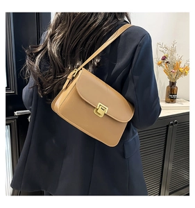 Brown leather crossbody bag with gold metal clasp shown on model in stylish lifestyle setting