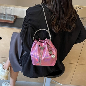 Pink laser bucket bag with metal handle and chain strap worn by model in a cafe