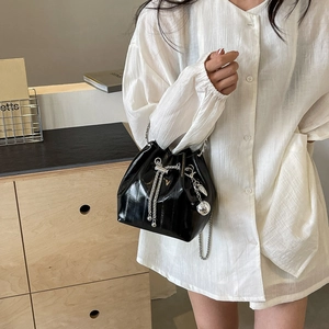 Glossy black bucket bag with water-ripple texture and silver chain drawstring on a model