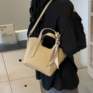 Minimalist beige bucket tote bag in litchi grain leather with decorative silk scarf handle