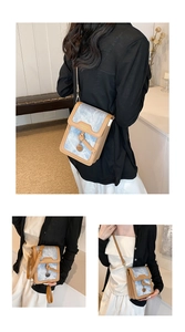 Detail of blue denim and brown leather crossbody bag with golden metal buckle and pendant