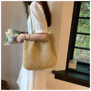 Detail of hand-woven straw tote bag showing intricate natural texture and long shoulder strap