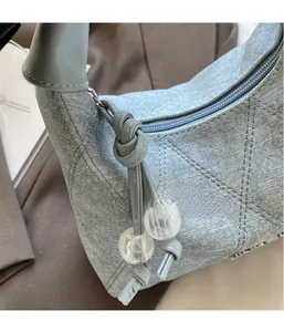 Close-up of light blue denim shoulder bag with quilted stitching and beaded knot detail