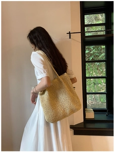 Detailed side view of a large straw tote bag worn by a model in a natural indoor setting
