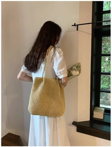 Detailed texture of a large beige straw tote bag carried by a model in a natural setting