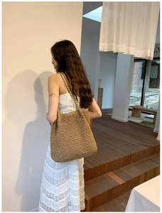 Detailed view of hand-woven straw tote bag with shoulder strap worn by a model