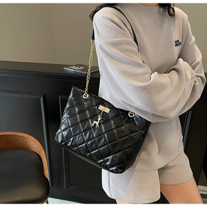 Detail of black quilted tote bag with gold chain strap and deer charm on a model