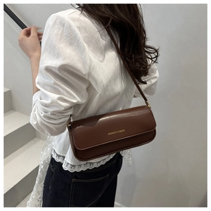 Détail du sac baguette marron foncé avec logo doré porté sur une chemise en dentelle