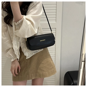 Gros plan sur un sac baguette en simili cuir noir avec lettrage doré porté à l'épaule